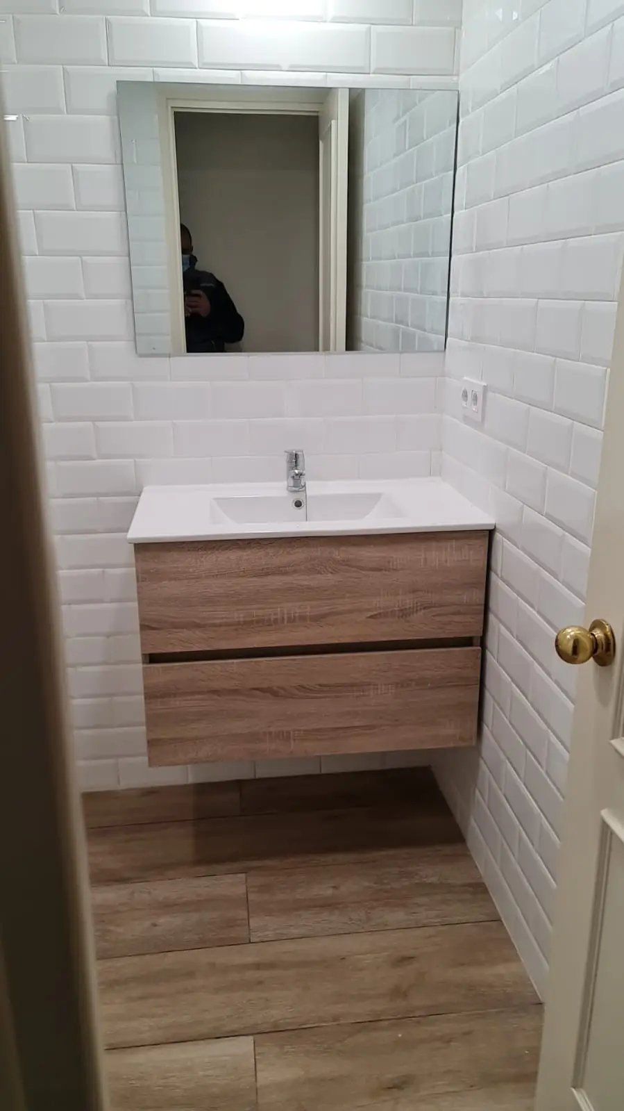 Baño reformado con azulejo metro blanco, mueble de lavabo suspendido en madera y suelo imitación madera