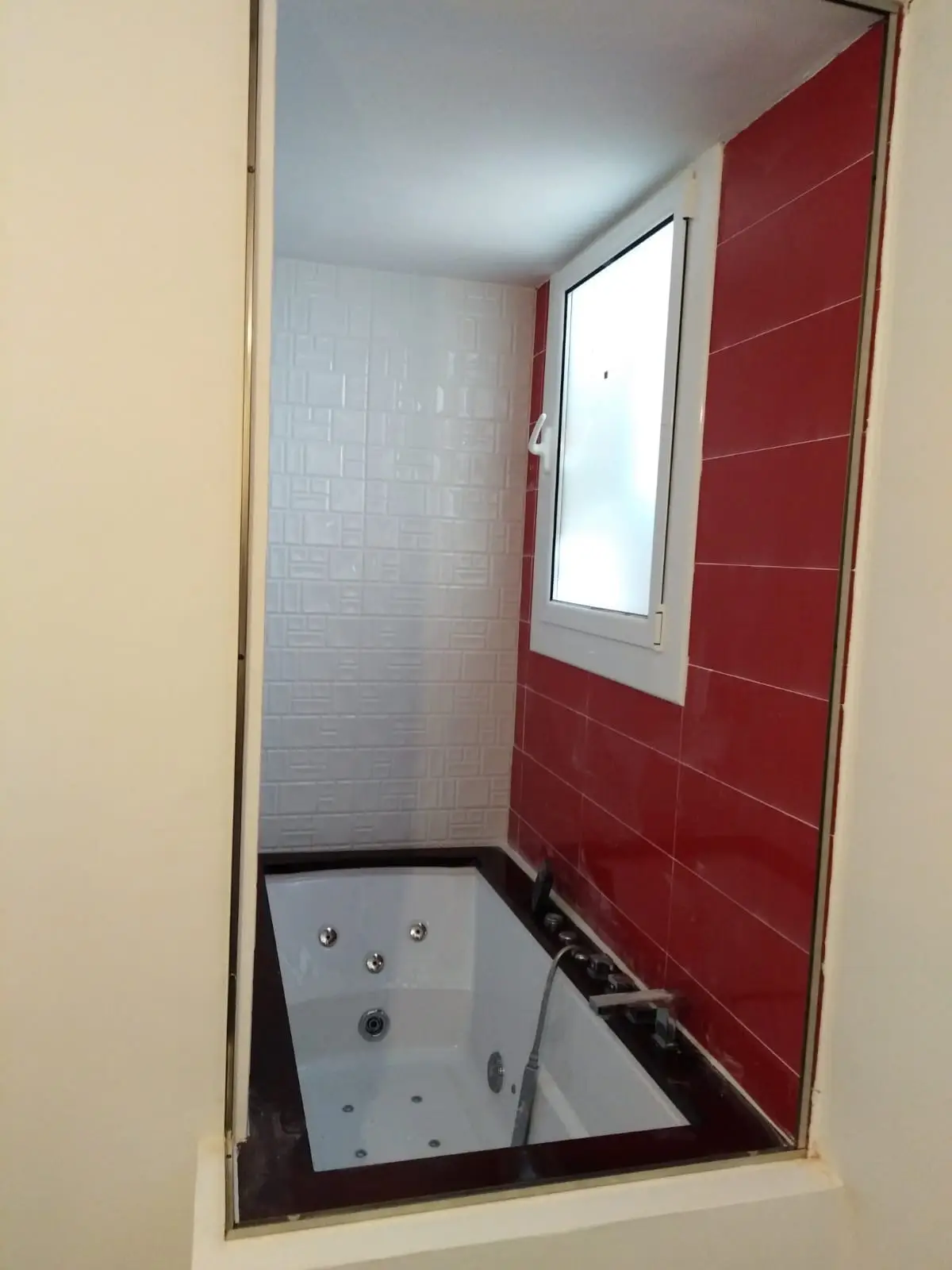 Baño con bañera de hidromasaje, azulejo rojo brillo y pared de azulejo blanco