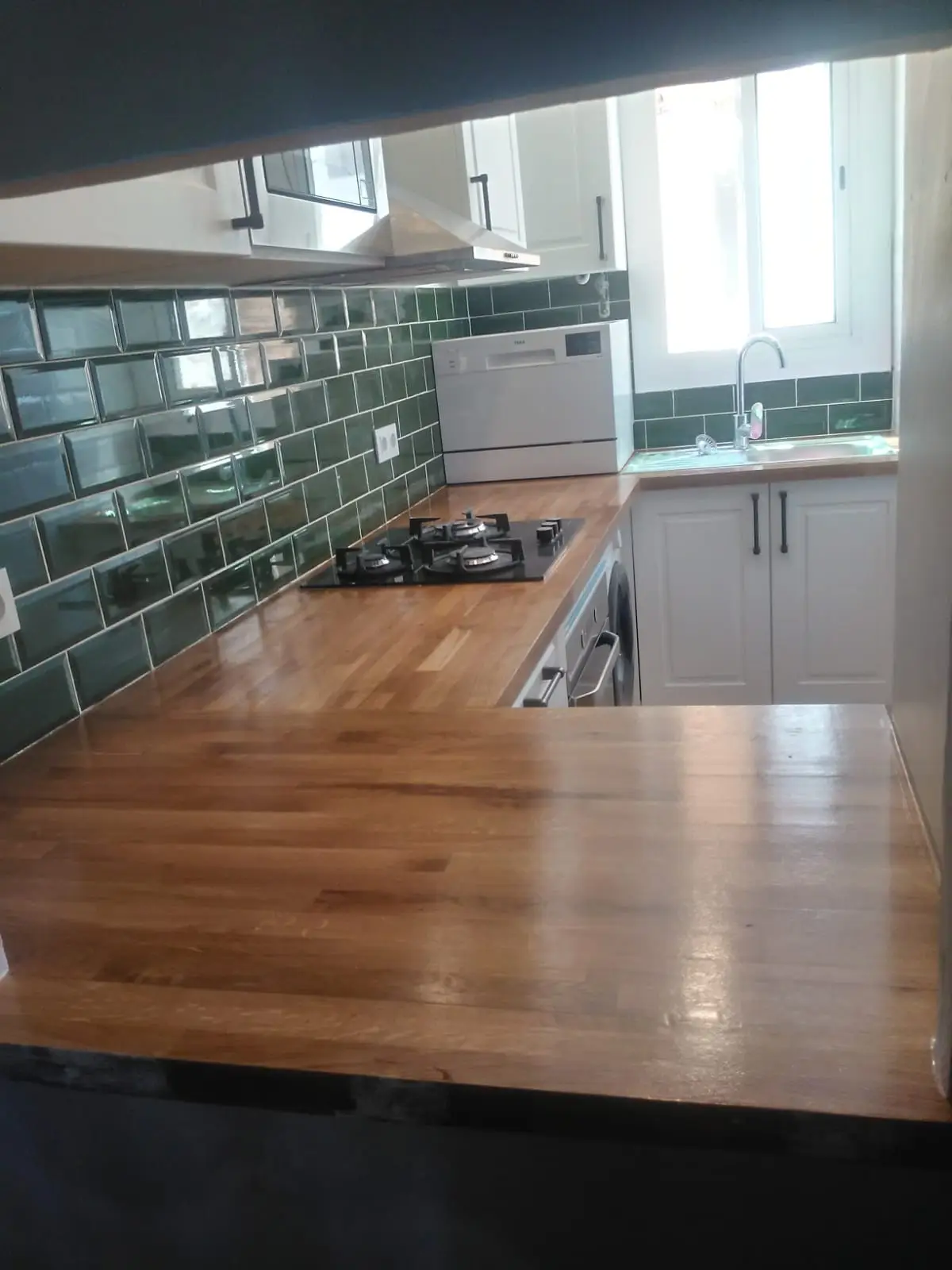 Cocina reformada con muebles blancos, encimera de madera maciza y frente de azulejo metro verde